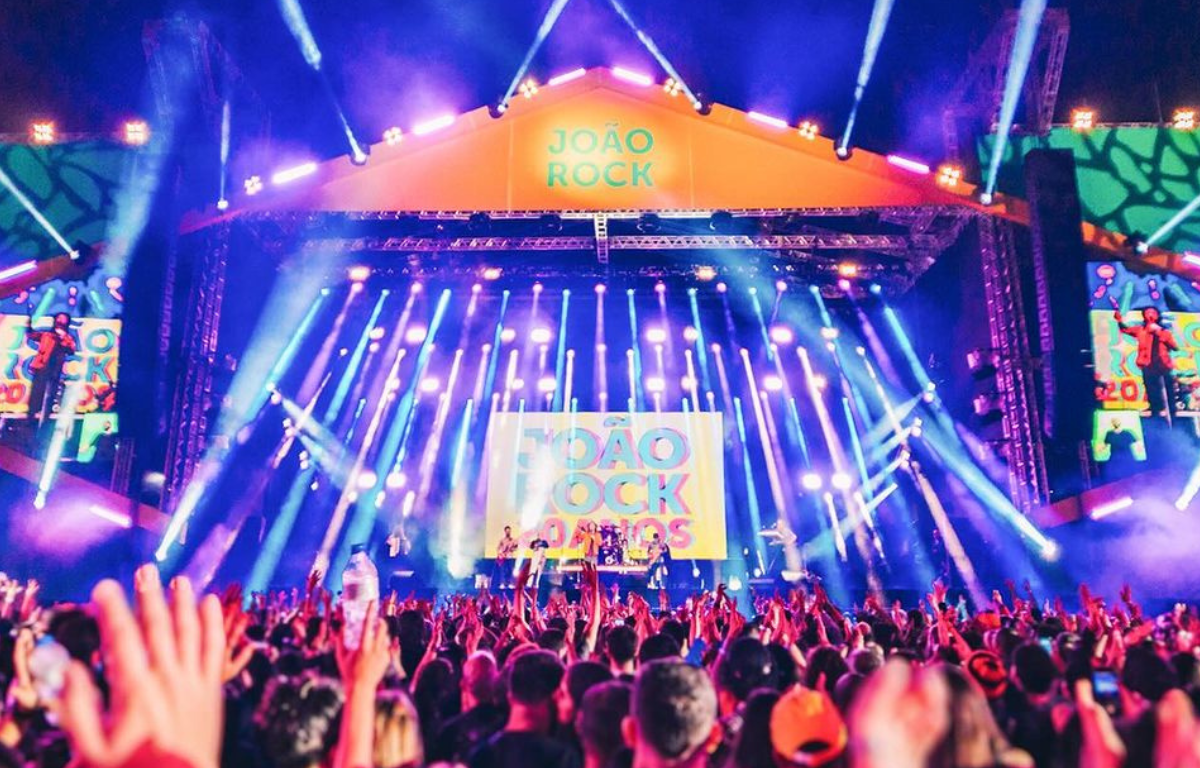 Público animado no Festival João Rock com palco iluminado e artistas se apresentando