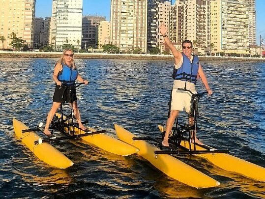 Bicicleta aquática em ação na Baixada Santista com vista para o mar e pessoas se divertindo.