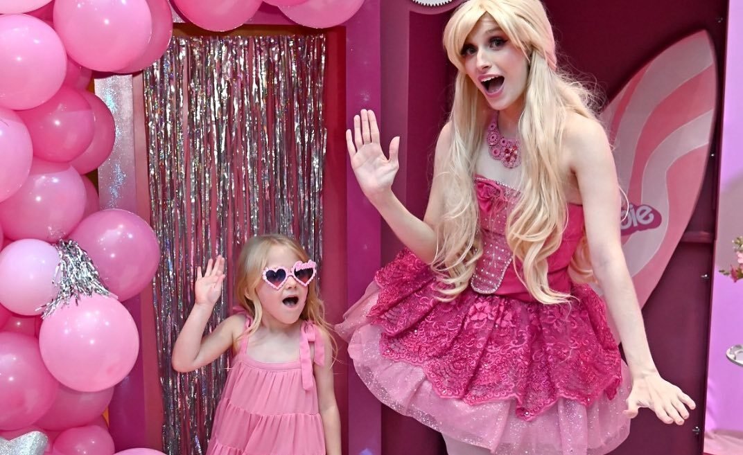 Crianças se divertindo no Chá das Bonecas em São Paulo, personalizando ecobags com a Barbie ao fundo.