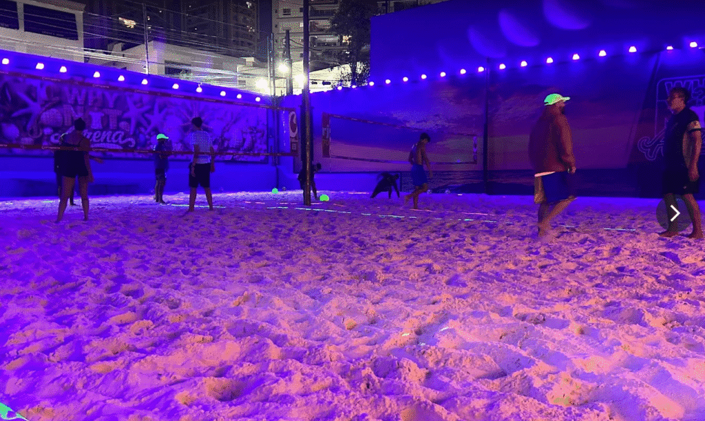 Quadra de beach tennis à noite em São Paulo com iluminação neon e pessoas jogando na WhyNot Arena