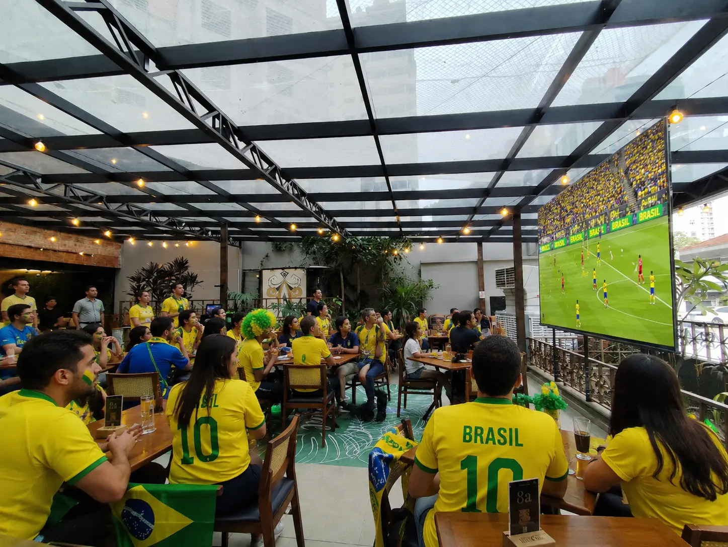 Família assistindo a um jogo de futebol em ambiente festivo no Quintal Del Carmem em Santo André, com telões de LED e decoração temática da Copa.