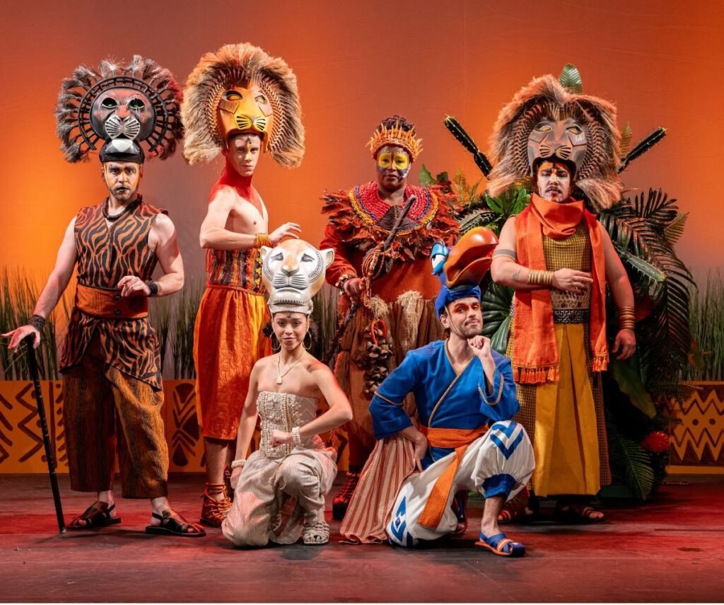 Cena do musical O Rei Leão no Teatro Multiplan, com Simba, Nala e outros personagens em um ambiente vibrante e colorido.